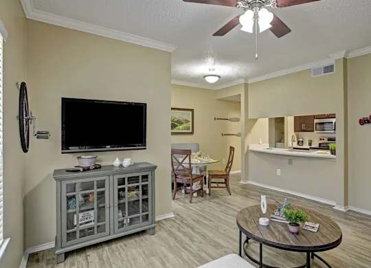 A living room with a grey cabinet, a black television, a ceiling fan, and a dining table with chairs.
