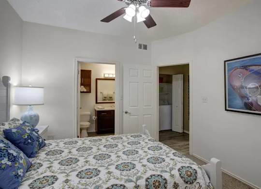 A bedroom with a patterned bedspread and a ceiling fan.