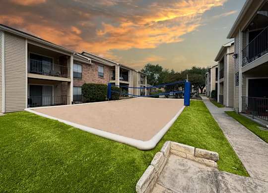 A skate park is located in the middle of a grassy area between two apartment buildings.