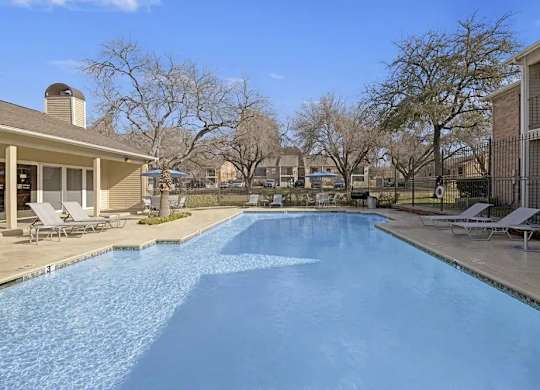 A swimming pool in a residential area with a house and trees in the background.