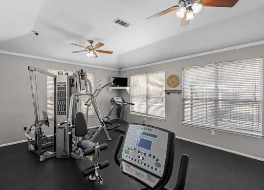 A home gym with a variety of exercise equipment and a ceiling fan.