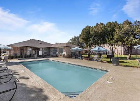 A swimming pool surrounded by lounge chairs and umbrellas in a sunny outdoor setting.