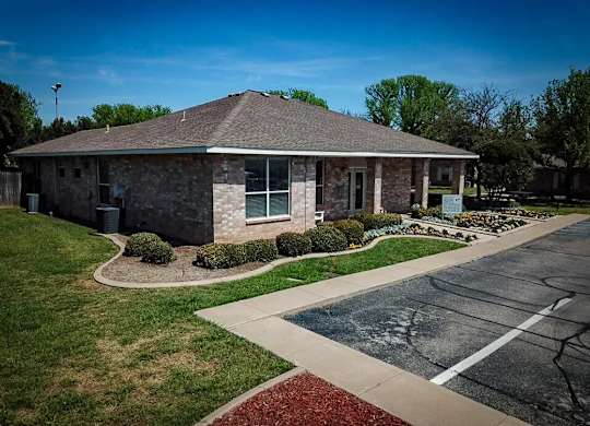A small building with a grey roof and a parking lot in front.