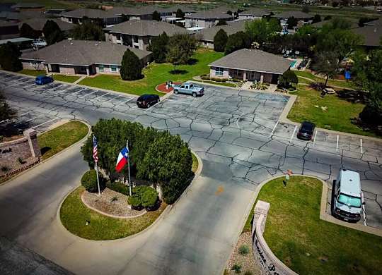 A residential street with cars parked on the side and a flagpole with the American and Texas flags.