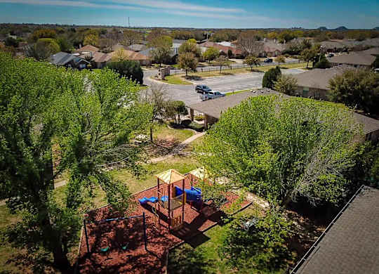 A playground with a swing set and a slide is surrounded by trees.