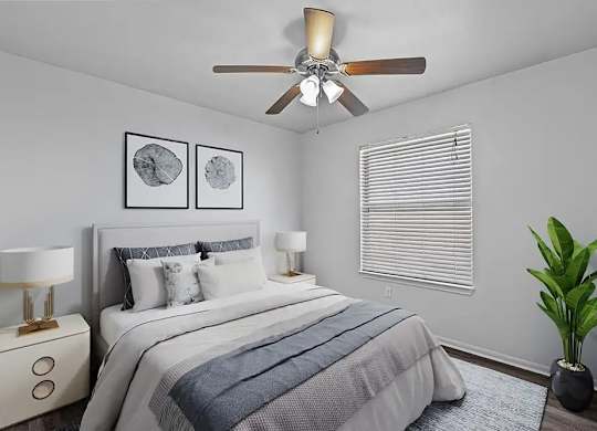 A bedroom with a bed, two lamps, a ceiling fan, and a plant.