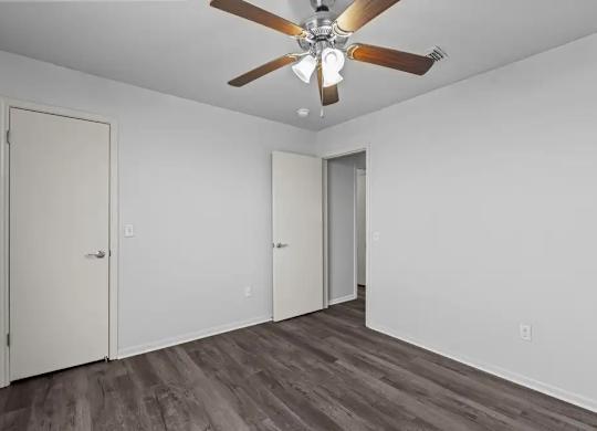 A room with a ceiling fan and wood flooring.