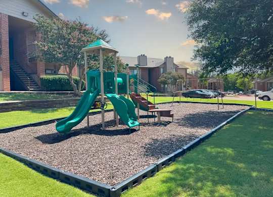 A playground with a green slide and a wooden bench.