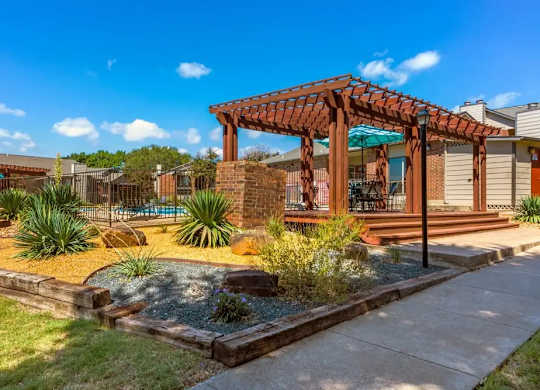 A wooden pergola is situated in a landscaped yard.
