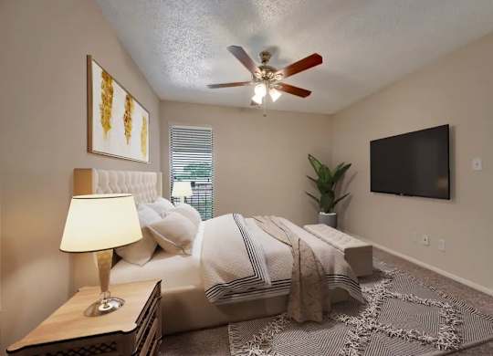 A bedroom with a bed, a ceiling fan, a lamp, a plant, and a television.