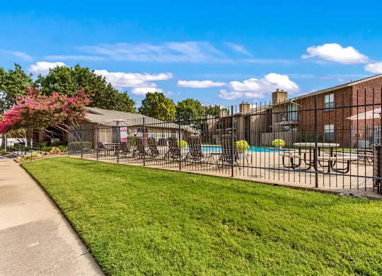 Fenced pool area with green lawn and buildings at South Meadows Apartments, Red Oak, 75154