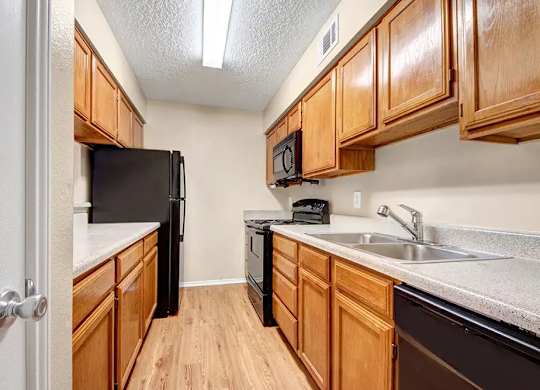 Galley kitchen with wood cabinets and black appliances at South Meadows Apartments, Red Oak, TX