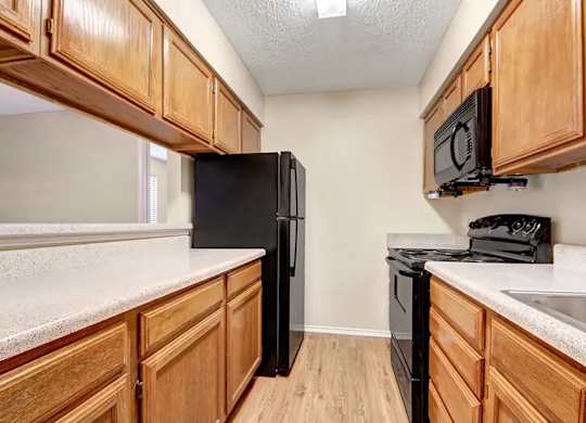 Galley kitchen with speckled countertops and black refrigerator at South Meadows Apartments, Red Oak, 75154