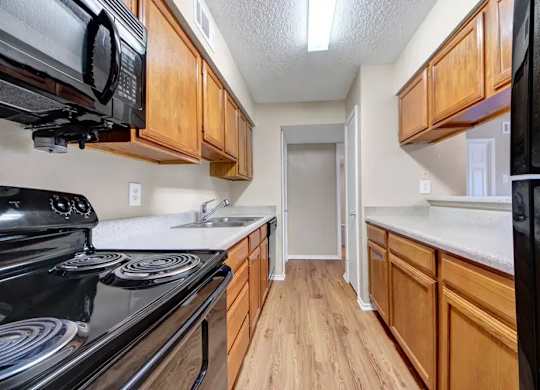 Galley kitchen with wood cabinetry and modern fixtures at South Meadows Apartments, Red Oak, Texas