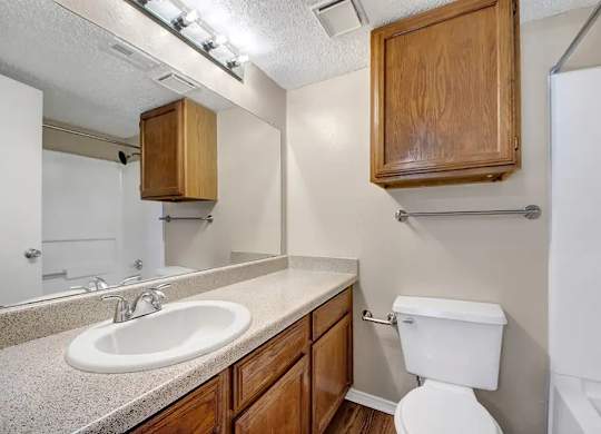 Bathroom with wood cabinets and speckled countertop at South Meadows Apartments, Texas, 75154