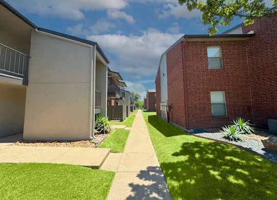 Walkway between apartment buildings with green lawns at South Meadows Apartments, Red Oak, 75154