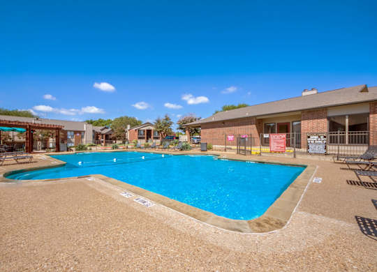 A large outdoor swimming pool surrounded by a sandy area and a few chairs.