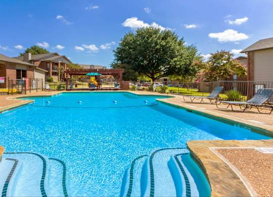 A large blue swimming pool with a wooden deck and lounge chairs.