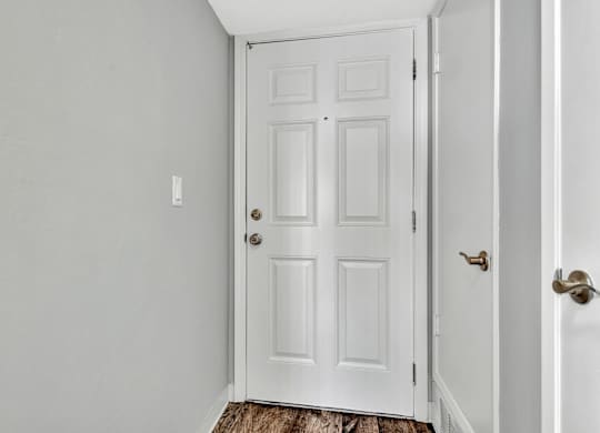 A white door with a brass handle is in a white room.