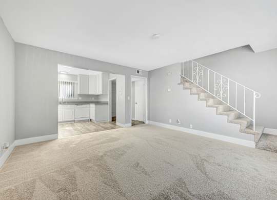 A spacious room with a staircase and a kitchen in the background.
