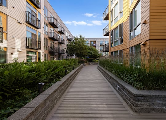 A long wooden walkway leads between two rows of modern apartment buildings.