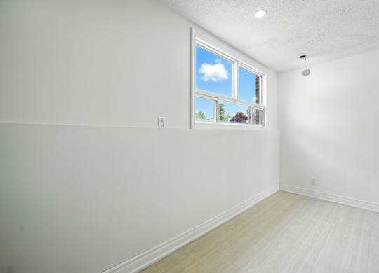 A room with a window showing a blue sky with clouds and greenery outside.
