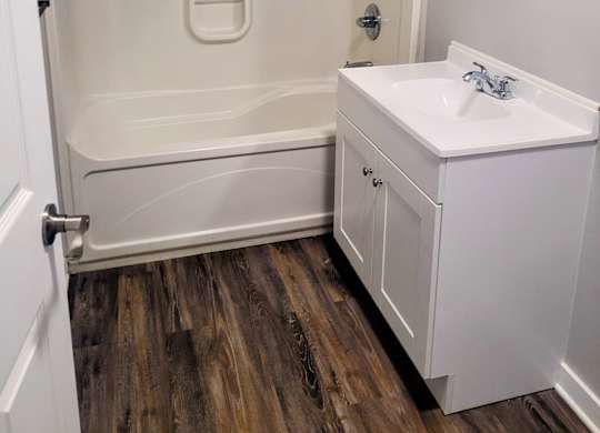 A white bathroom with a wooden floor and a white sink.