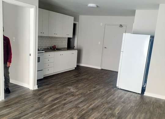 A person stands in a kitchen with white cabinets and a white refrigerator.