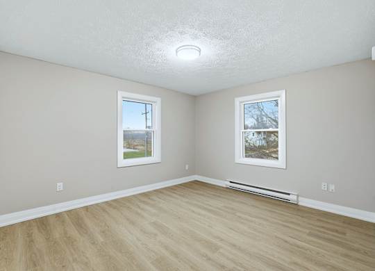 A room with light wood flooring and two windows.