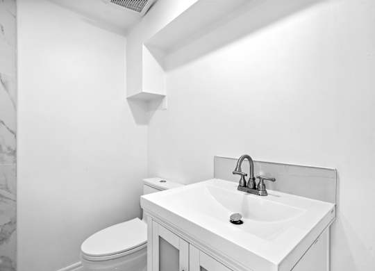 A white bathroom with a toilet, sink, and a marble wall.