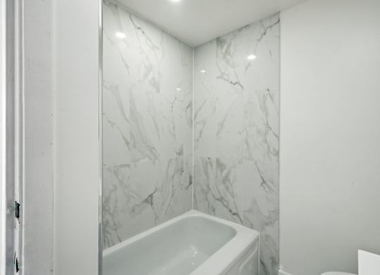 A white bathroom with a marble wall and a white tub.