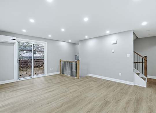 A spacious room with a wooden floor and a staircase on the right side.