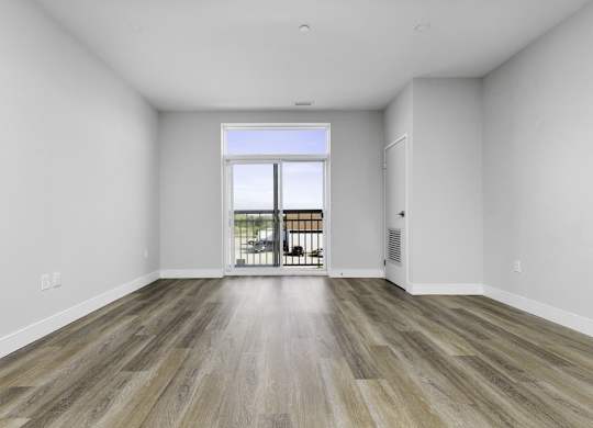 A room with a wooden floor and a sliding glass door leading to a balcony.