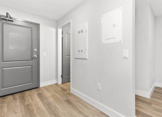 A room with a grey door and a white wall with a switchboard.