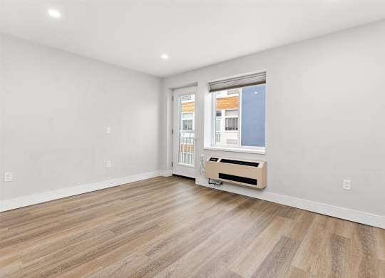 A room with a wooden floor and a window with a view of a building outside.