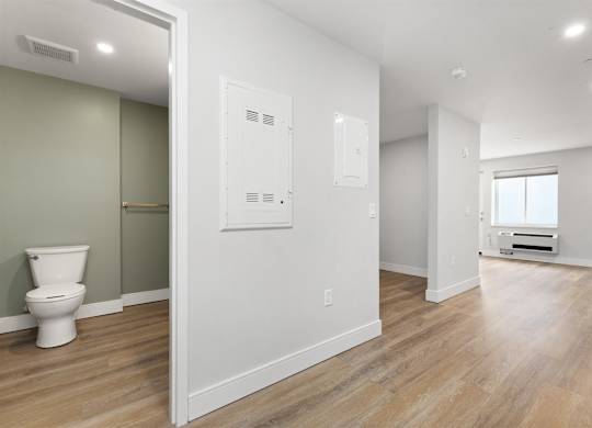 A white toilet sits in a room with wood floors and white walls.