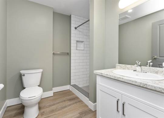A white toilet sits in a bathroom with a marble counter and a shower with a glass door.