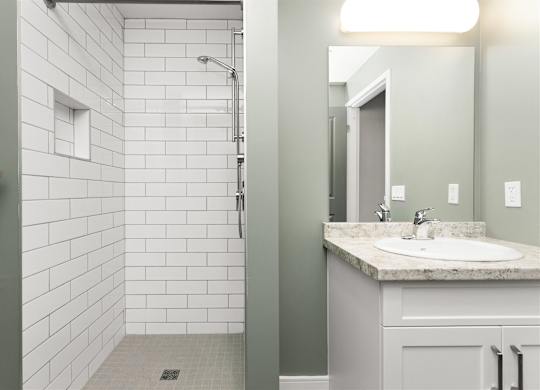 A bathroom with a white tiled shower and a sink with a marble countertop.