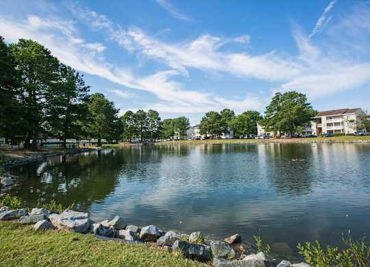 A serene lake surrounded by trees and a building in the distance under a clear blue sky.