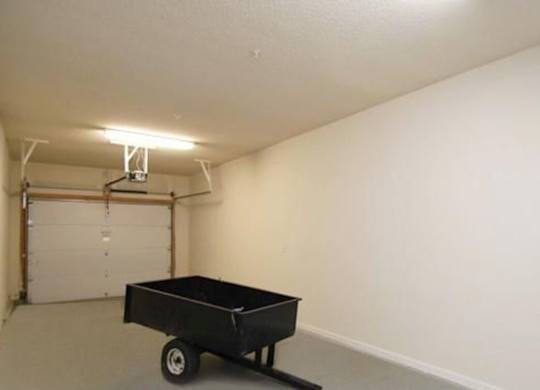 A black wheelbarrow is in the middle of a white room.