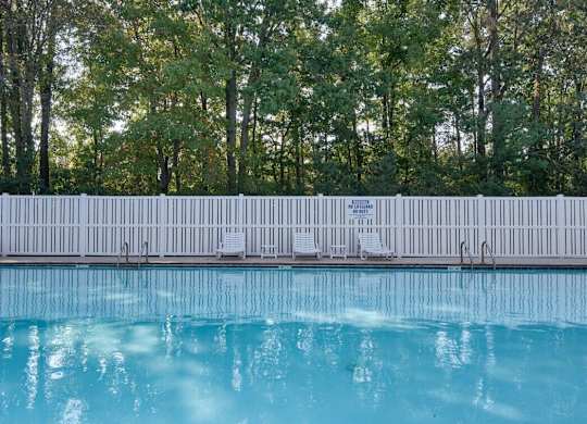 A pool with a white fence and trees in the background.