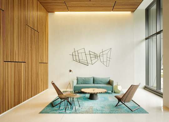 A modern living room with a blue rug and a large abstract metal sculpture on the wall.