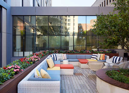 A patio with a couch and chairs is surrounded by flowers.
