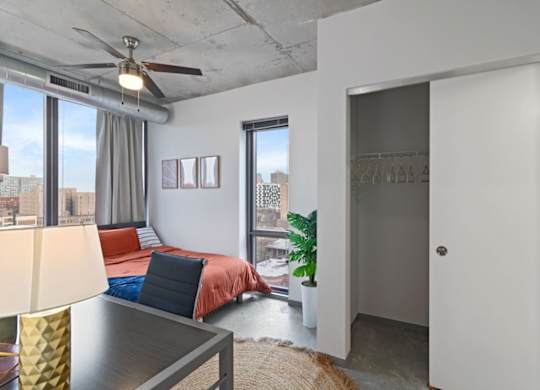 A bedroom with a bed, a ceiling fan, and a view of the city.