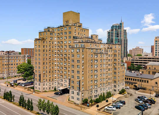 A large tan building with a green roof sits in the middle of a parking lot.