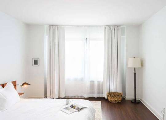 A white bedroom with a large bed and a window with curtains.