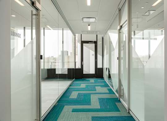 A hallway with glass walls and a blue carpet.