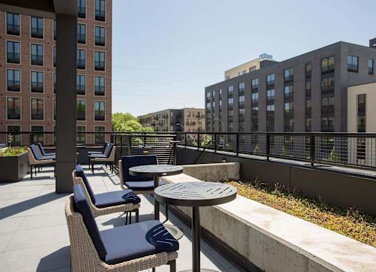 A patio with chairs and tables is surrounded by buildings.