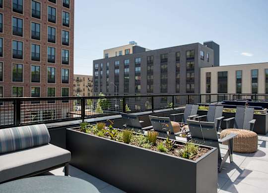 A rooftop patio with a planter box and chairs.