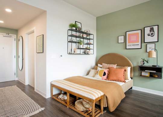 A bedroom with a bed, a rug, and a wall-mounted shelf.